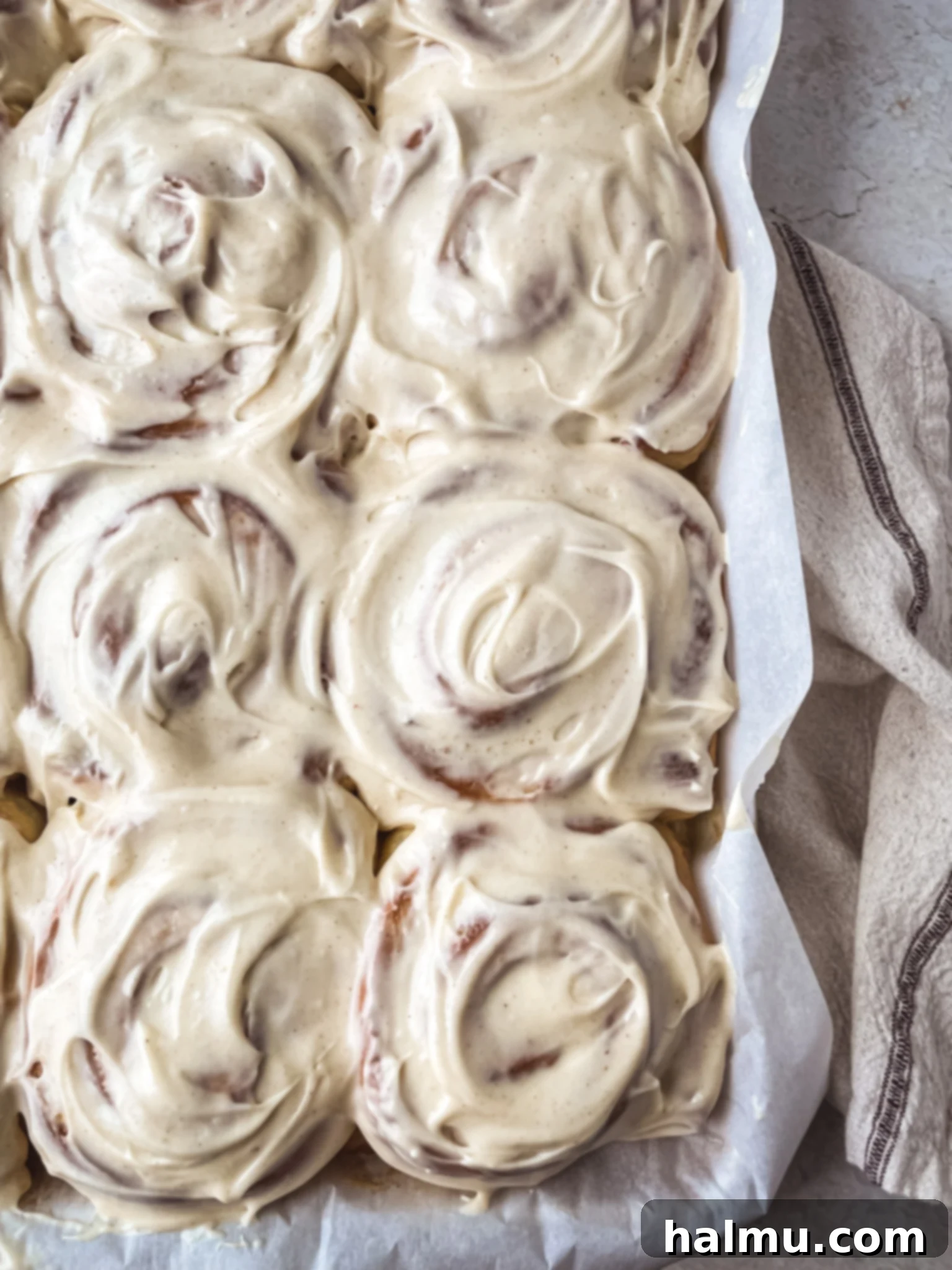Golden Brown Butter Brioche Cinnamon Swirls 2 Close-up of three golden-brown brioche cinnamon rolls topped with a generous swirl of cream cheese frosting, showing the gooey center and browned butter flecks.