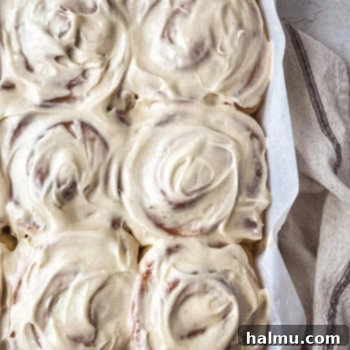 Golden Brown Butter Brioche Cinnamon Swirls 10 Close-up of three golden-brown brioche cinnamon rolls topped with a generous swirl of cream cheese frosting.