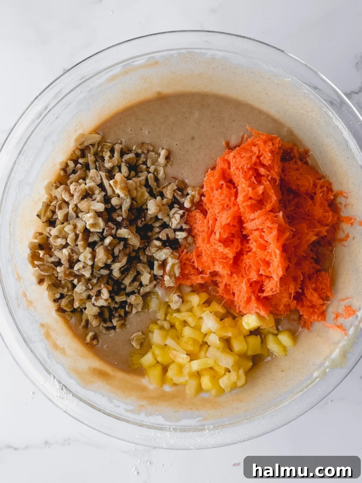 Mixing bowl with carrot cake batter, carrots, pineapple, and walnuts visible