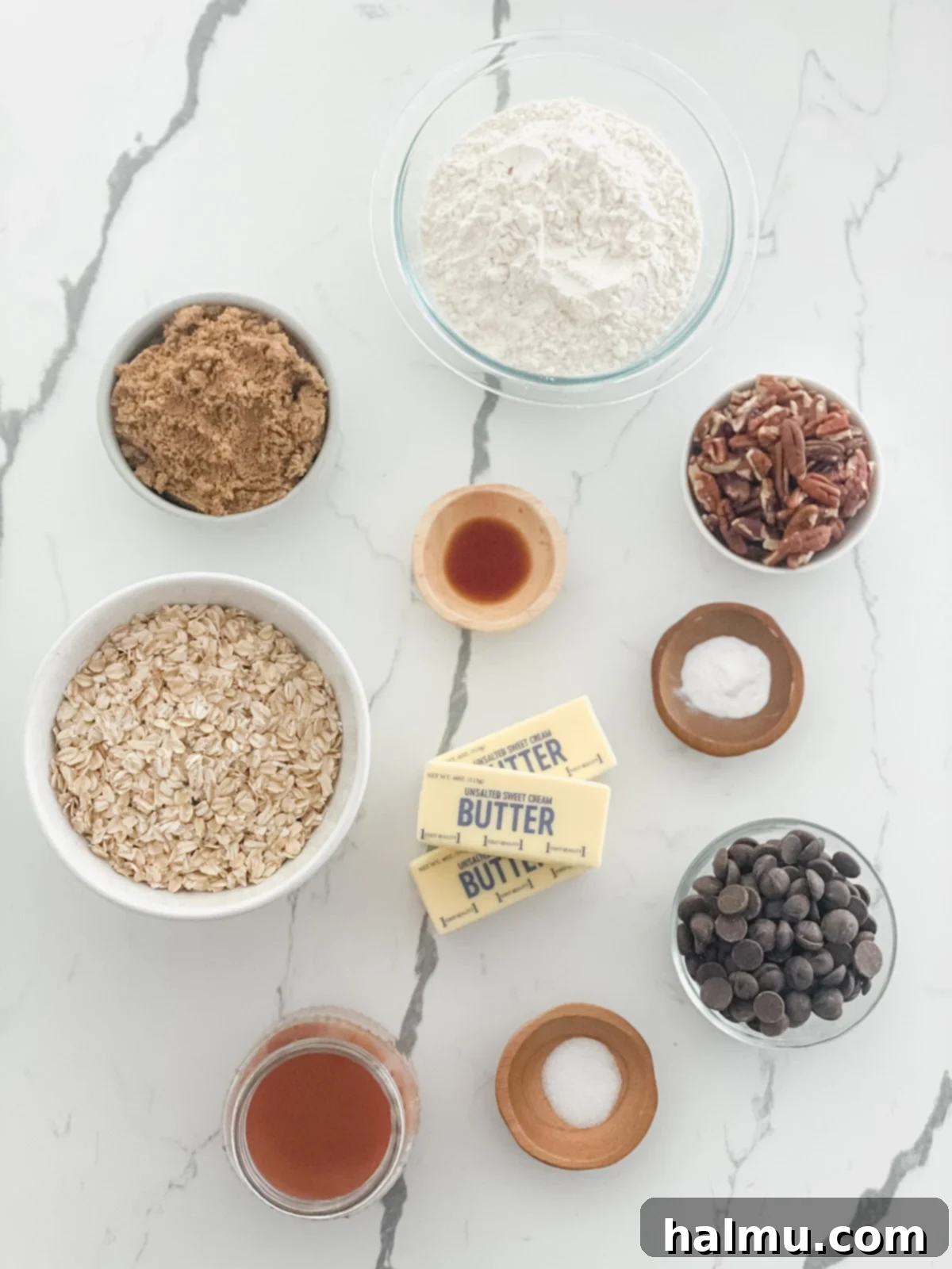 A close-up of the gooey caramel being spread over the oat base in a baking pan, with chopped pecans and chocolate chips ready to be added.