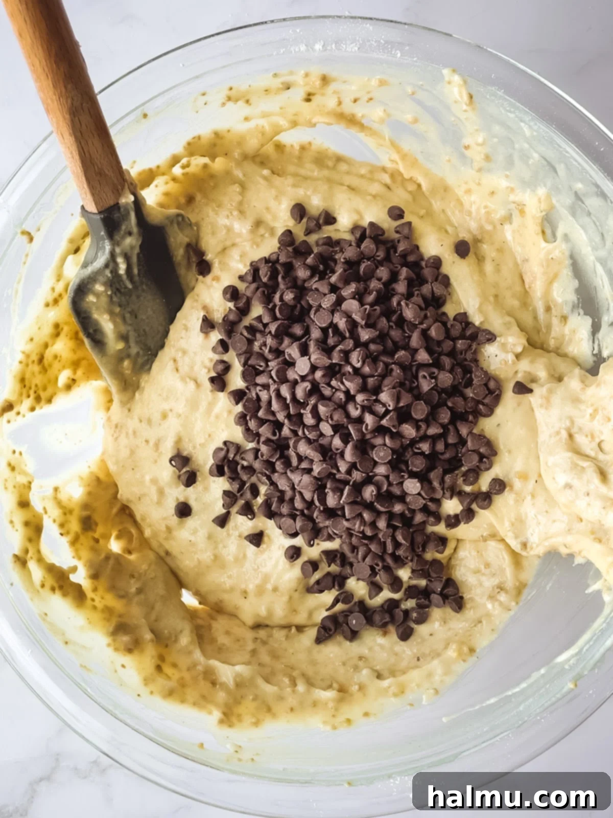 Muffin batter being scooped into tulip liners in a muffin pan.