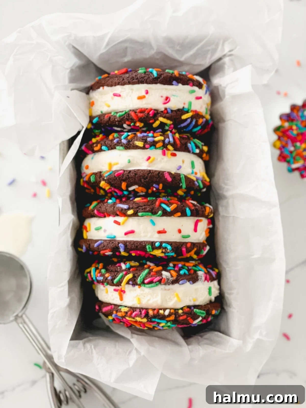 Chocolate Sprinkle Cookie Ice Cream Stacks 3 A hand holding a chocolate sprinkle cookie ice cream sandwich, with a vibrant blue background.