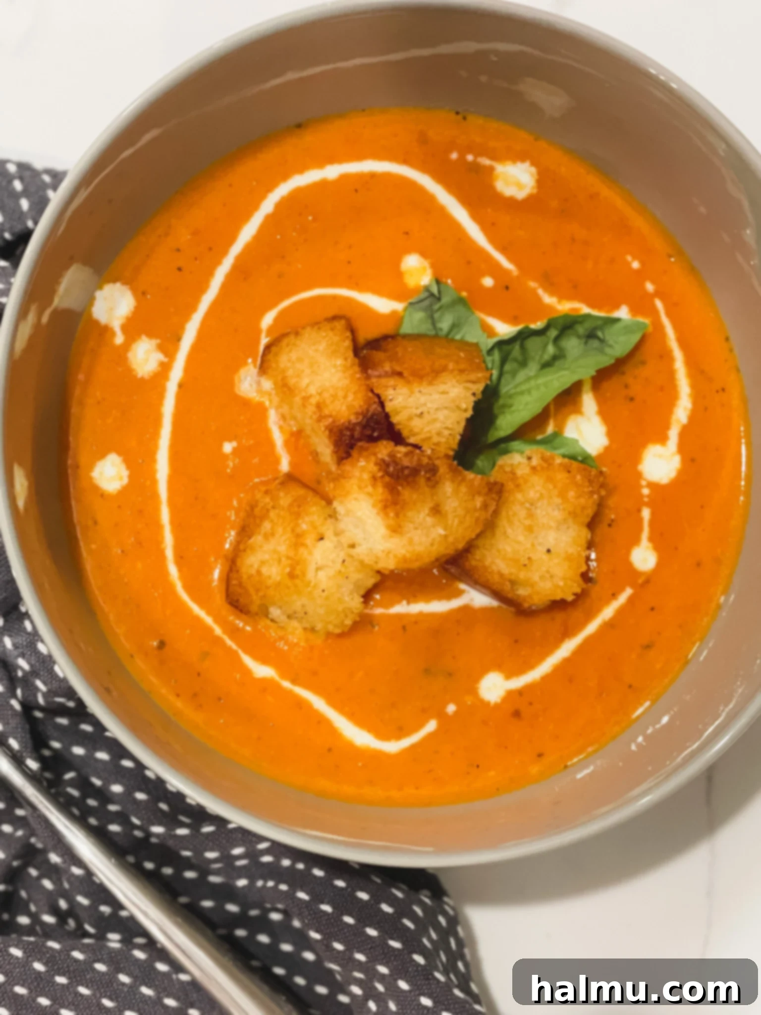 A large pot of creamy tomato basil soup garnished with fresh basil leaves.