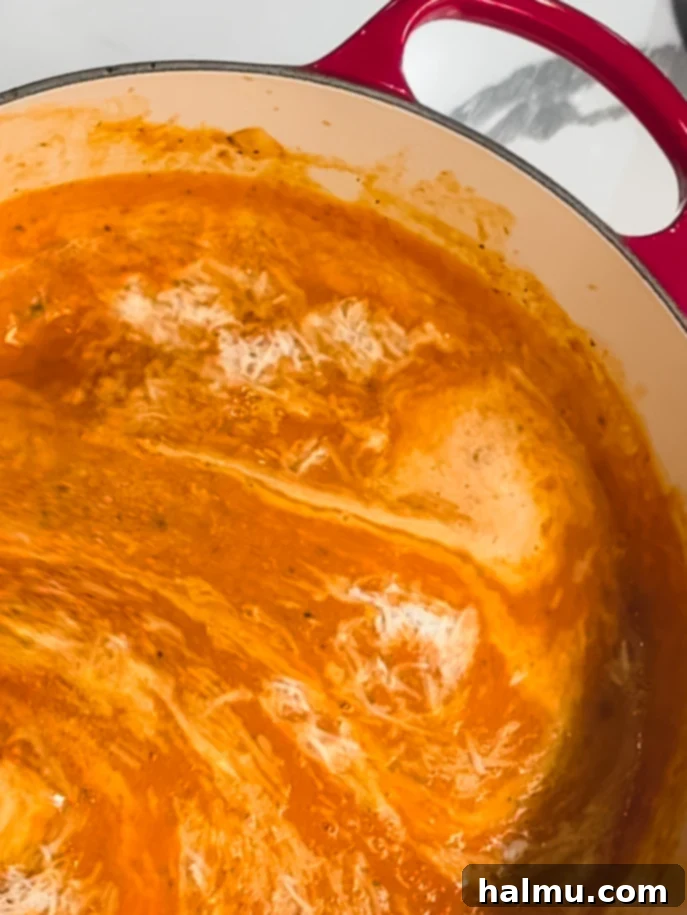 A close-up of a bowl of creamy tomato basil soup with a swirl of cream and fresh basil.