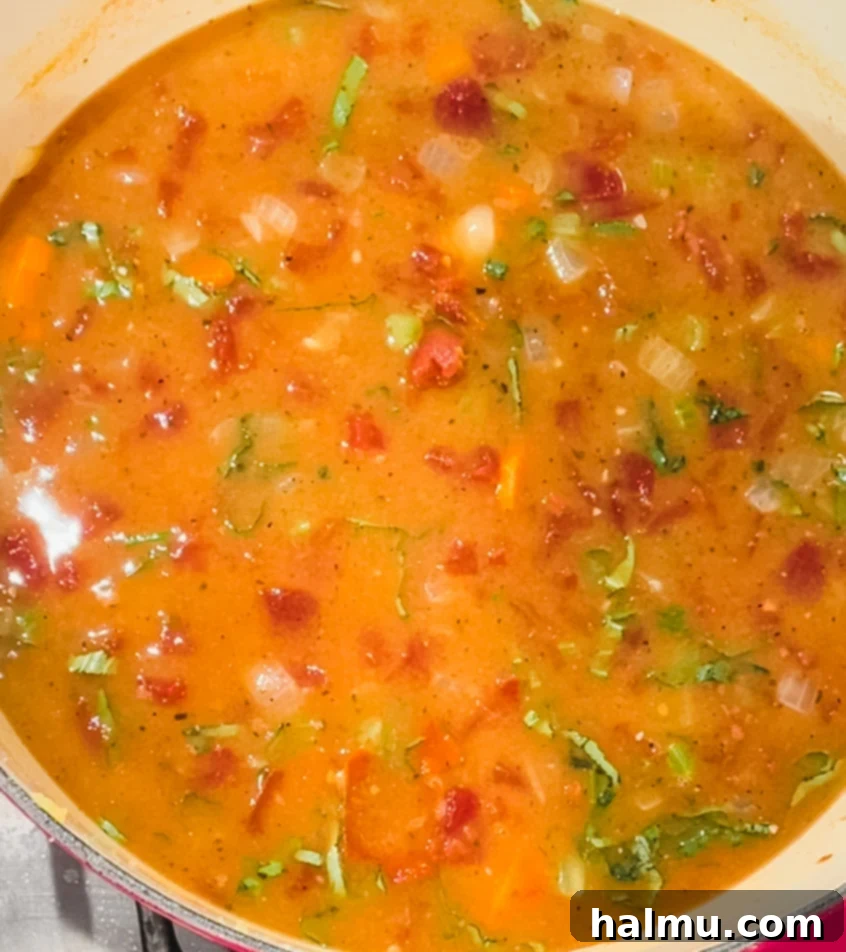 A bowl of creamy tomato basil soup with a grilled cheese sandwich cut in half.