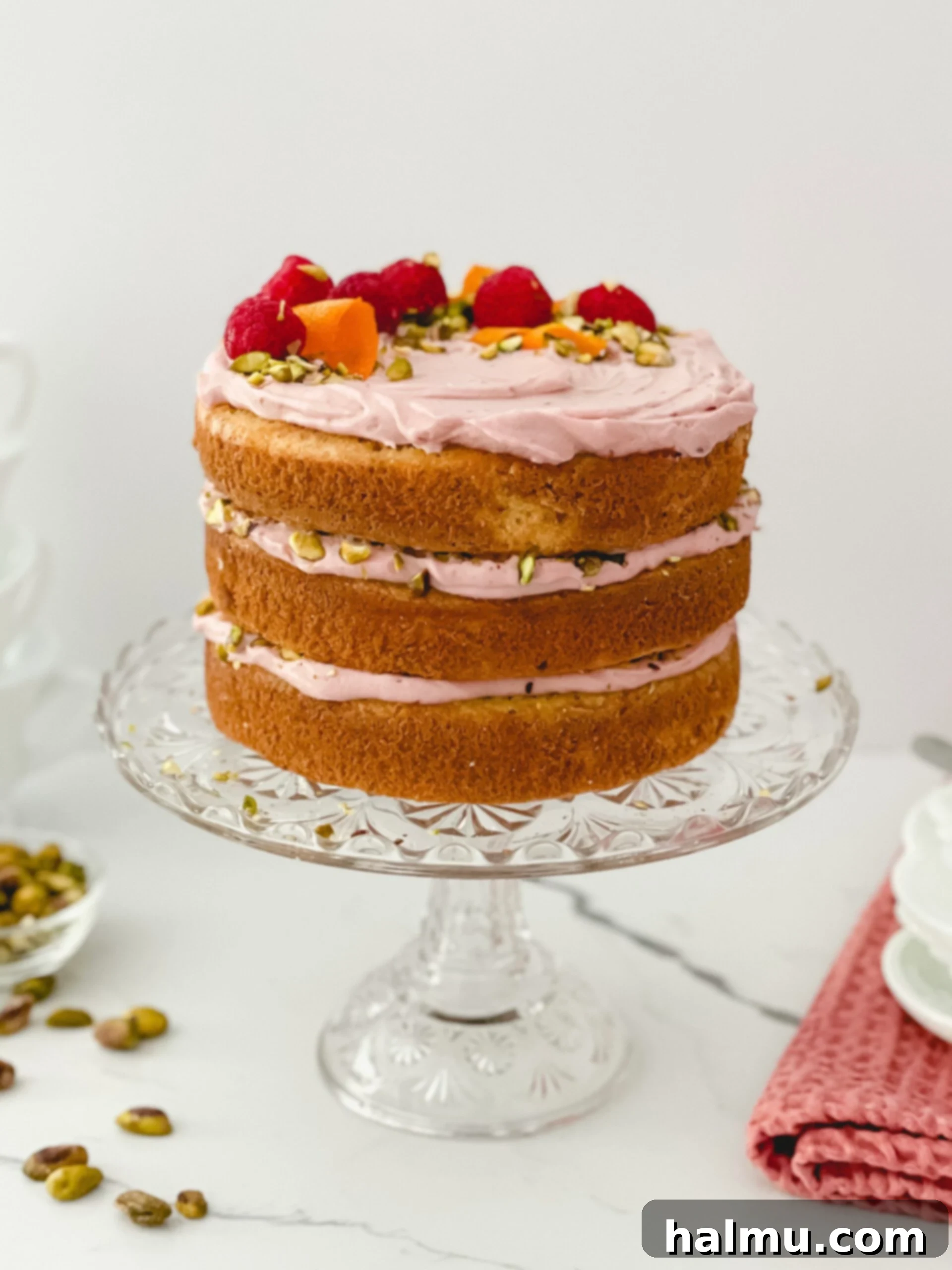 A beautifully layered Raspberry Orange Pistachio Cake, showcasing delicate pink raspberry whipped cream, green pistachios, and orange zest.