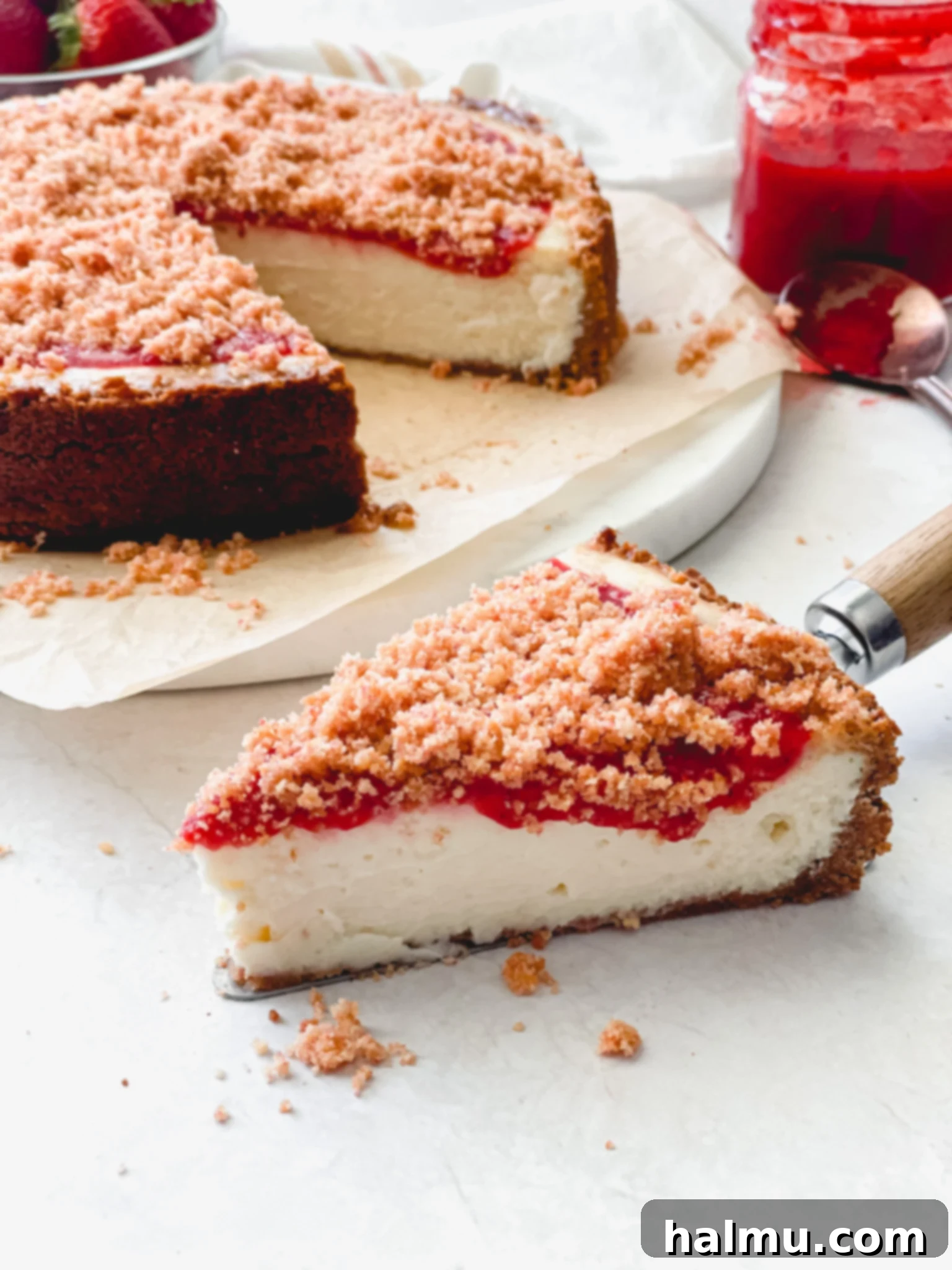 A slice of Strawberry Crunch Cheesecake with strawberry sauce and crumble topping.