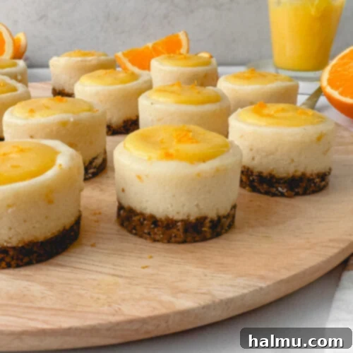 A vibrant close-up of a mini orange cheesecake, garnished with fresh orange zest and a mint leaf, highlighting its intricate layers and appealing presentation.