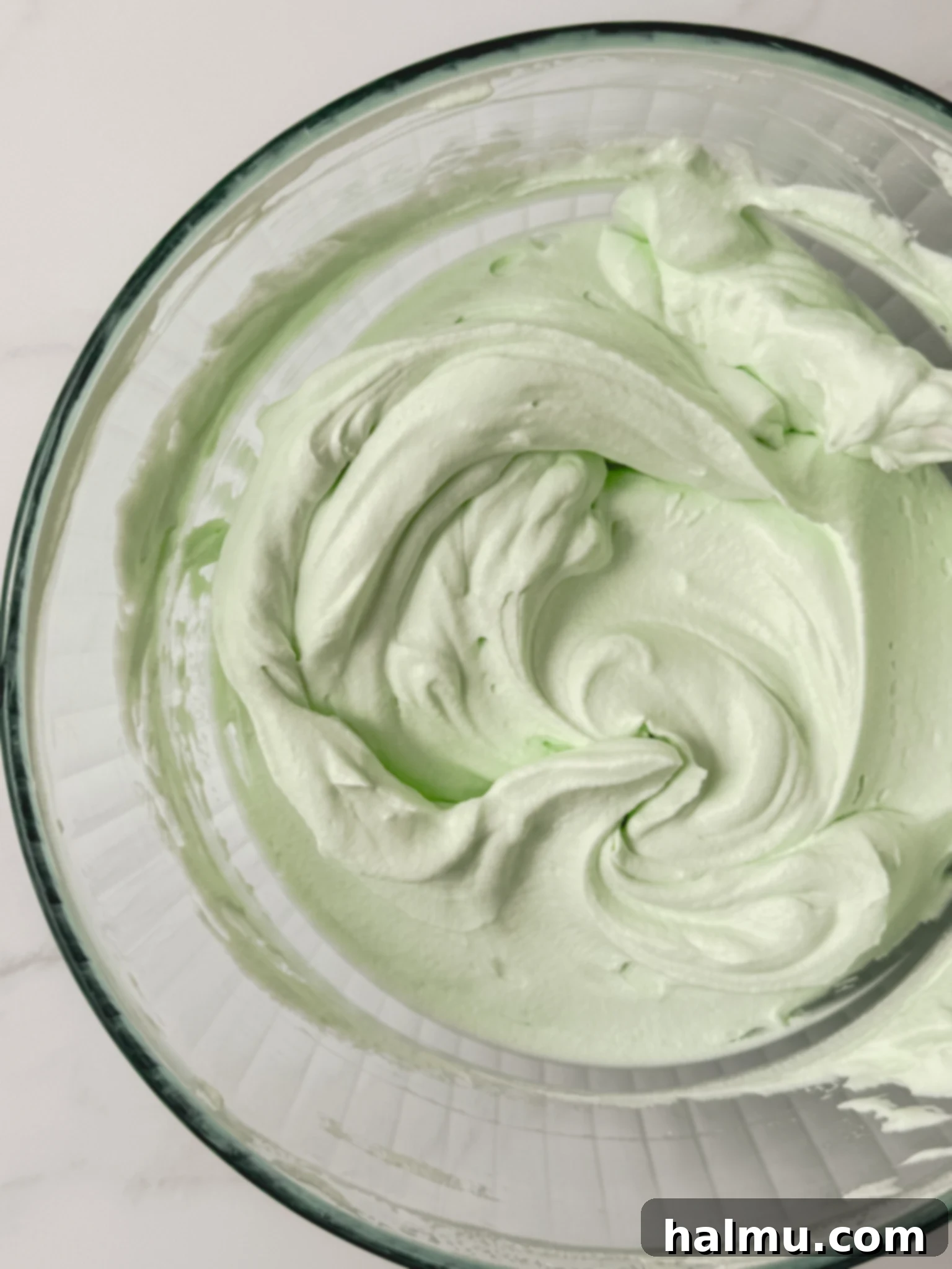 Mint green whipped cream, fluffy and ready, in a stand mixer bowl with a whisk attachment.