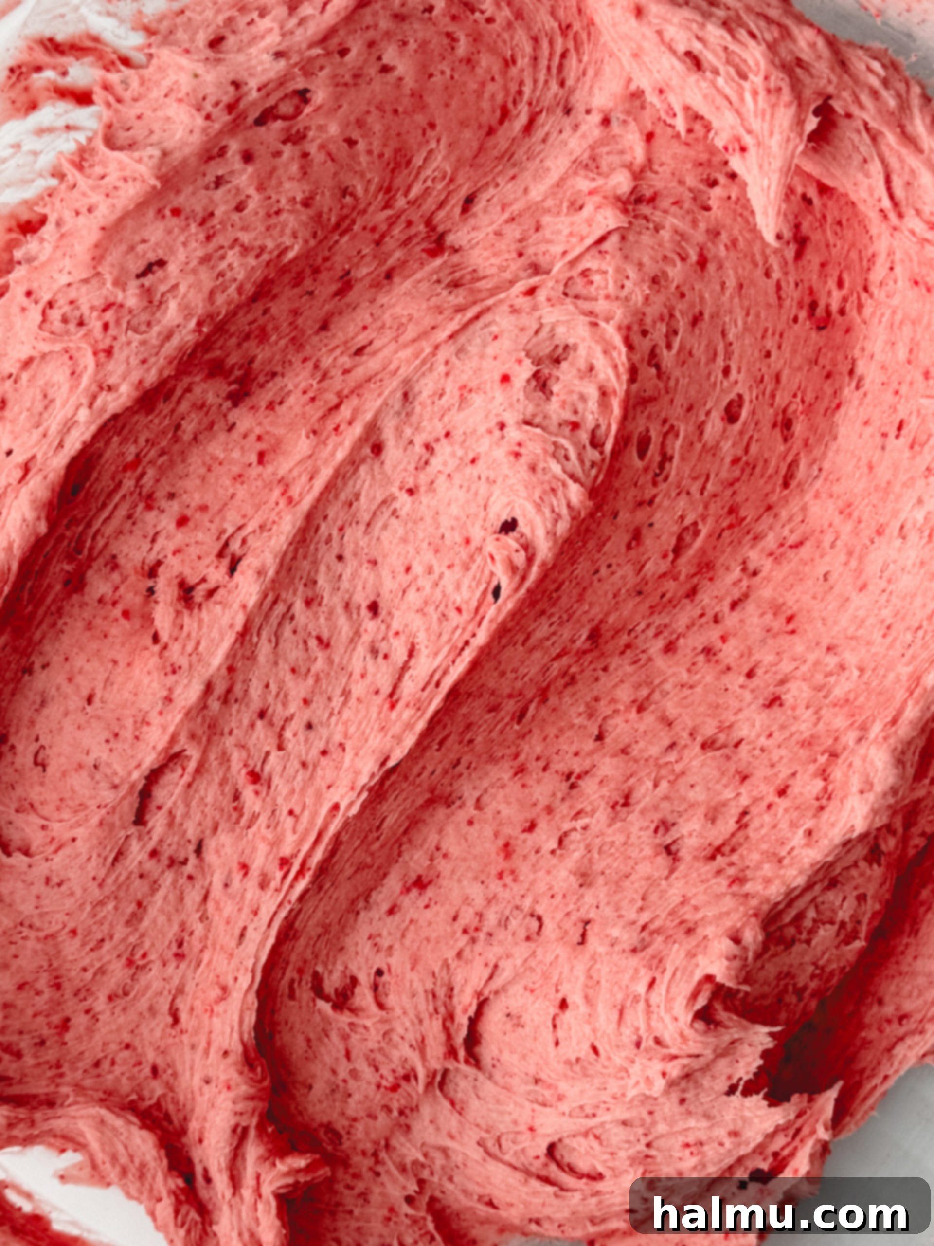 A close-up of a spoon dipping into smooth, pink strawberry buttercream in a bowl.