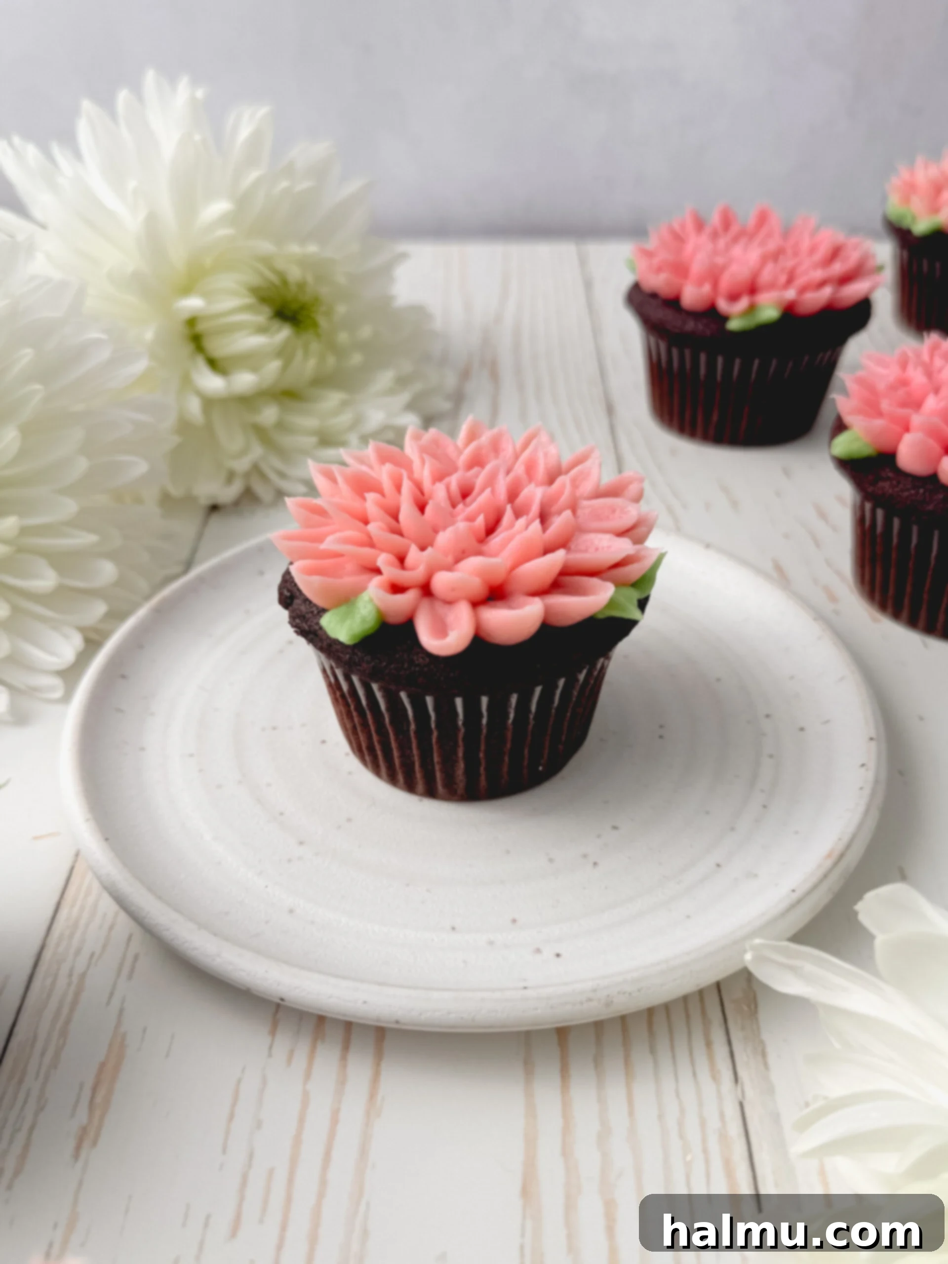 Cupcake Candles 3 Overhead shot of beautifully piped two-toned pink mum cupcakes with green leaves on a white background, showcasing intricate buttercream detail.