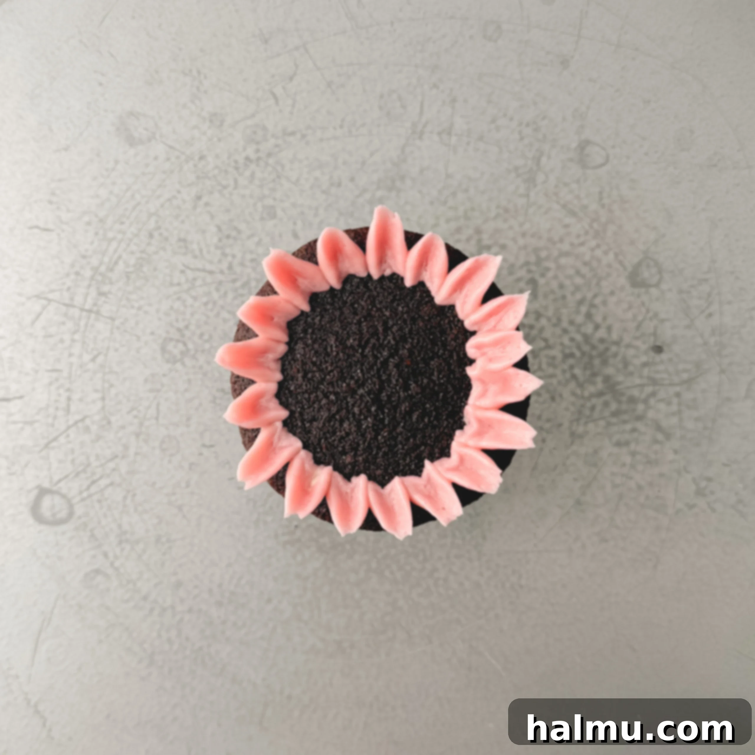 Cupcake Candles 5 Image showing the first ring of buttercream petals being piped around the outer edge of a chocolate cupcake using a mum tip at a 45-degree angle.