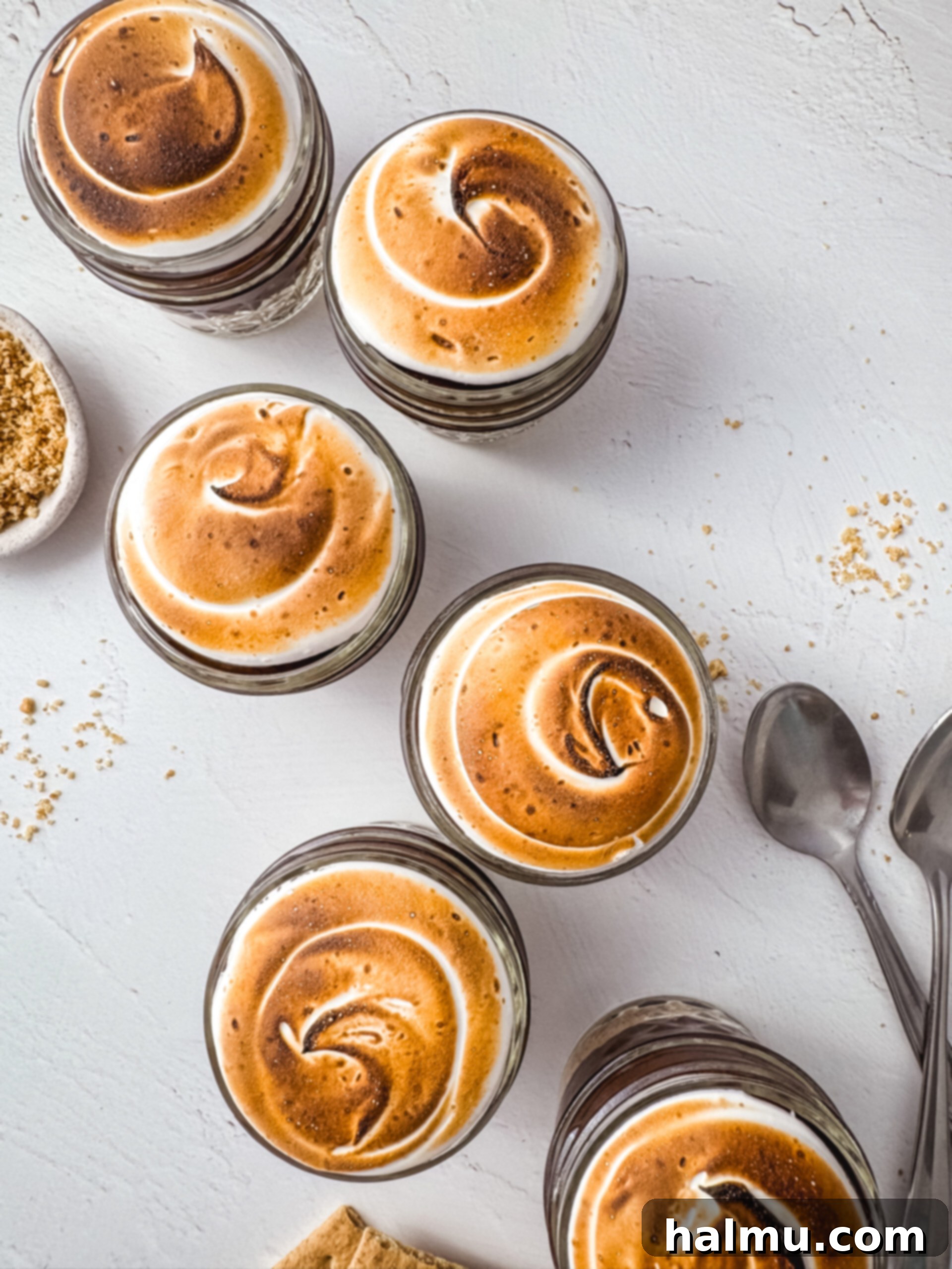 Decorating S'more Pudding Cups with piped marshmallow meringue and toasting it with a kitchen torch.