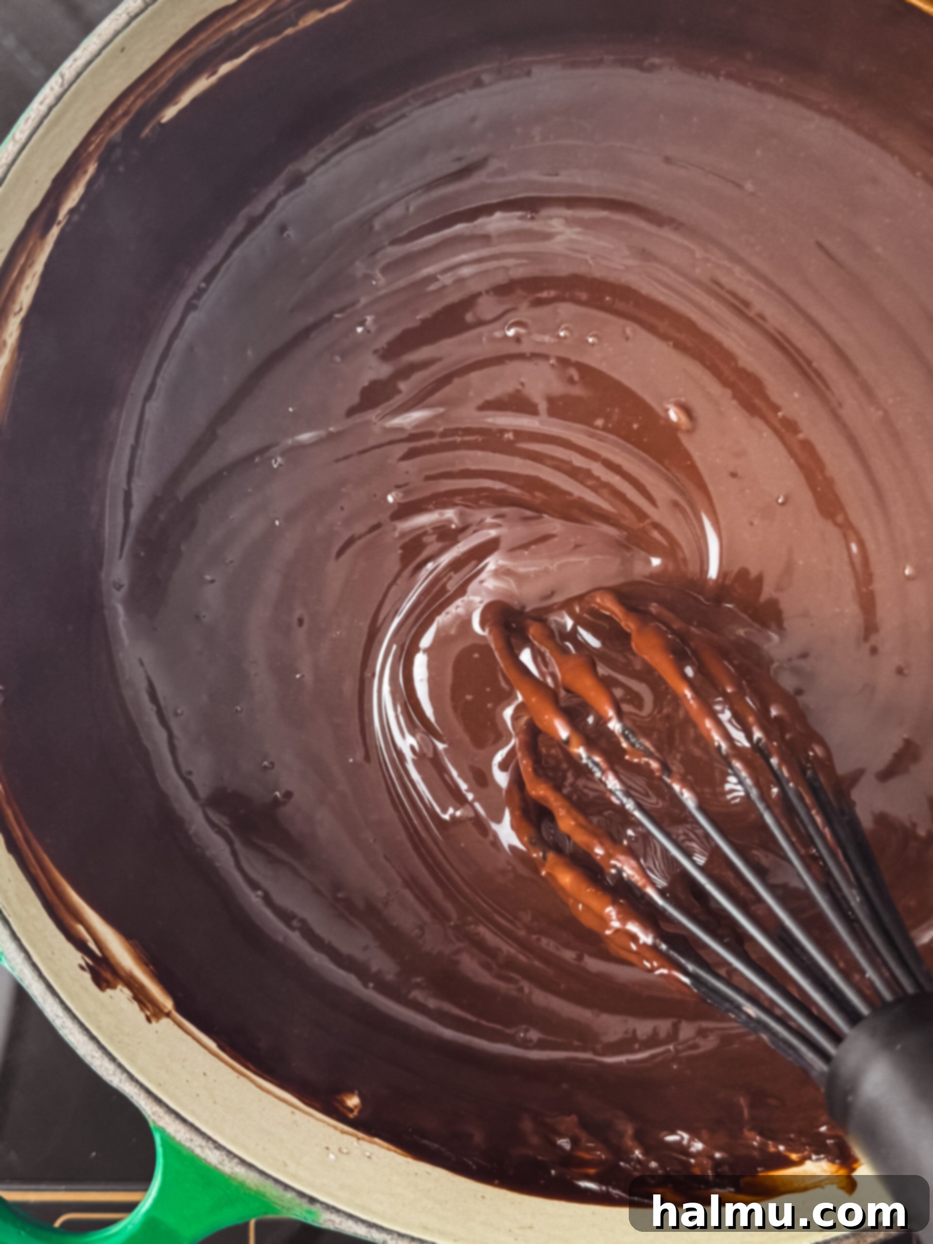 Thickening chocolate pudding being continuously whisked in a saucepan on the stove.