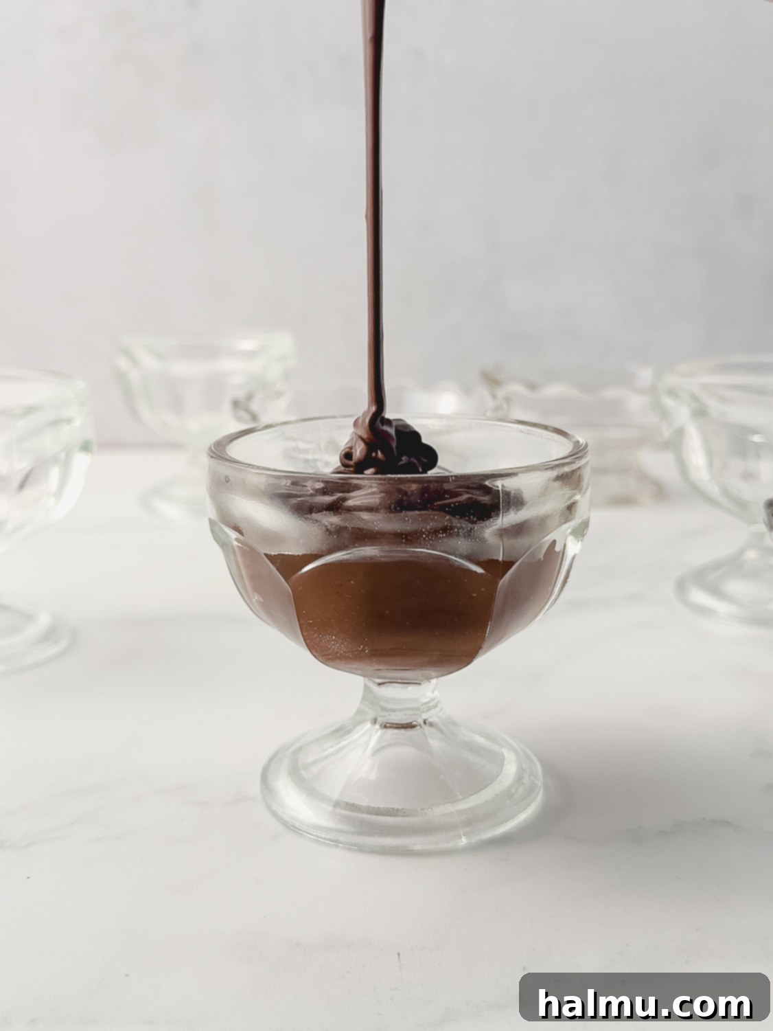 Straining freshly cooked homemade chocolate pudding through a fine mesh sieve into a glass bowl.