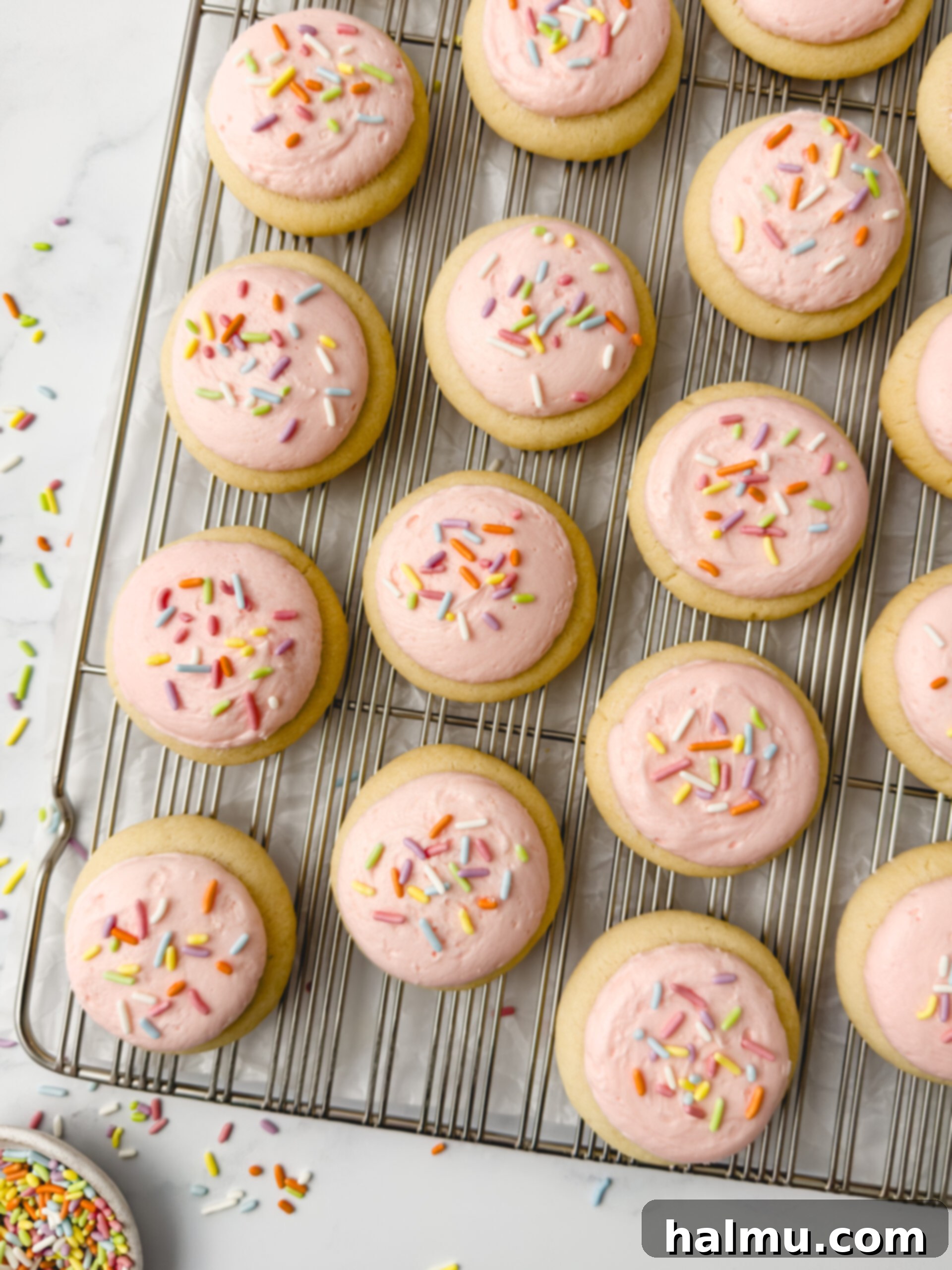 Finished mini frosted sugar cookies with sprinkles on a plate.