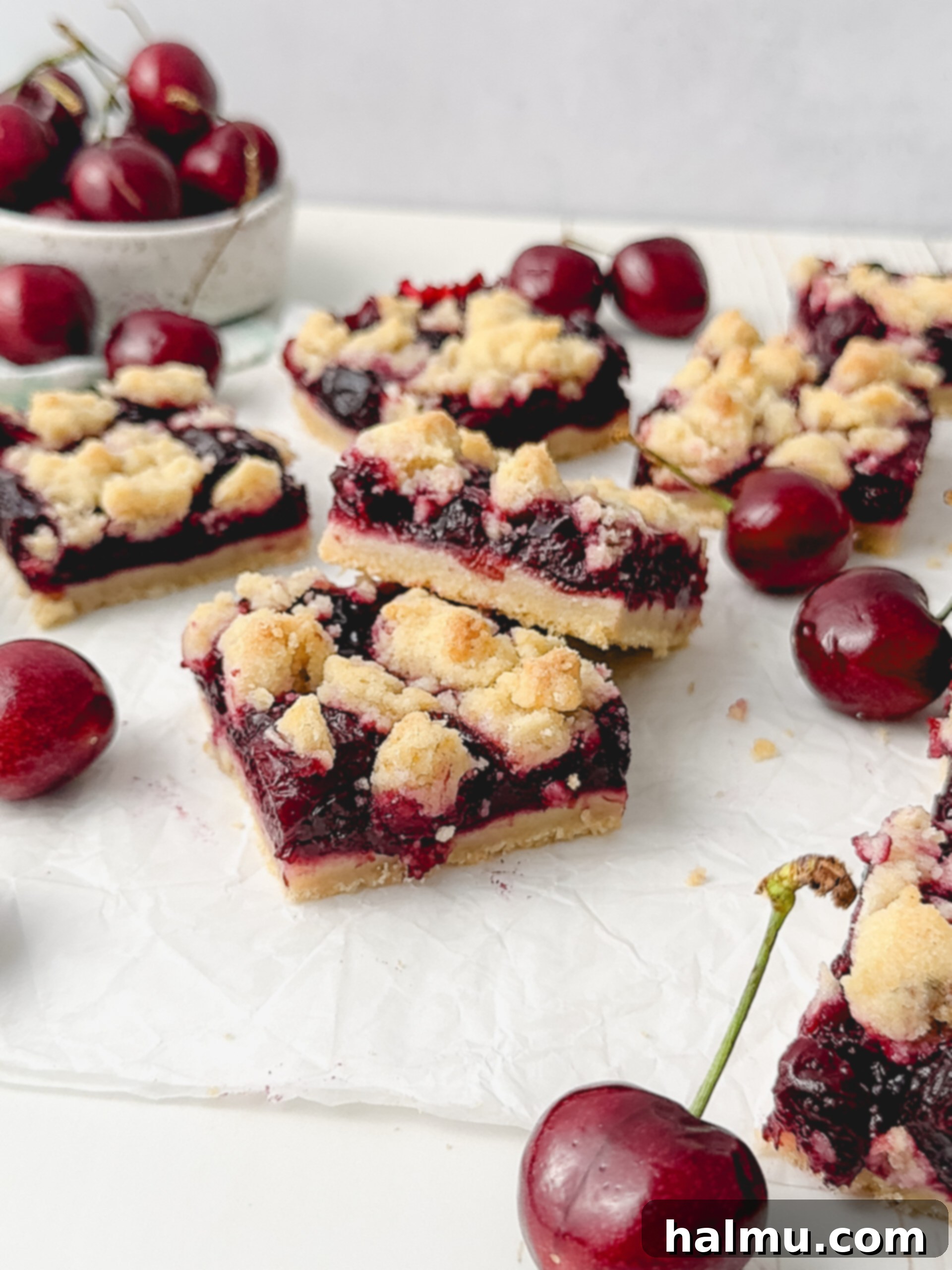 Overhead shot of two cherry crumb bars on a plate with fresh cherries and a small glass of milk.