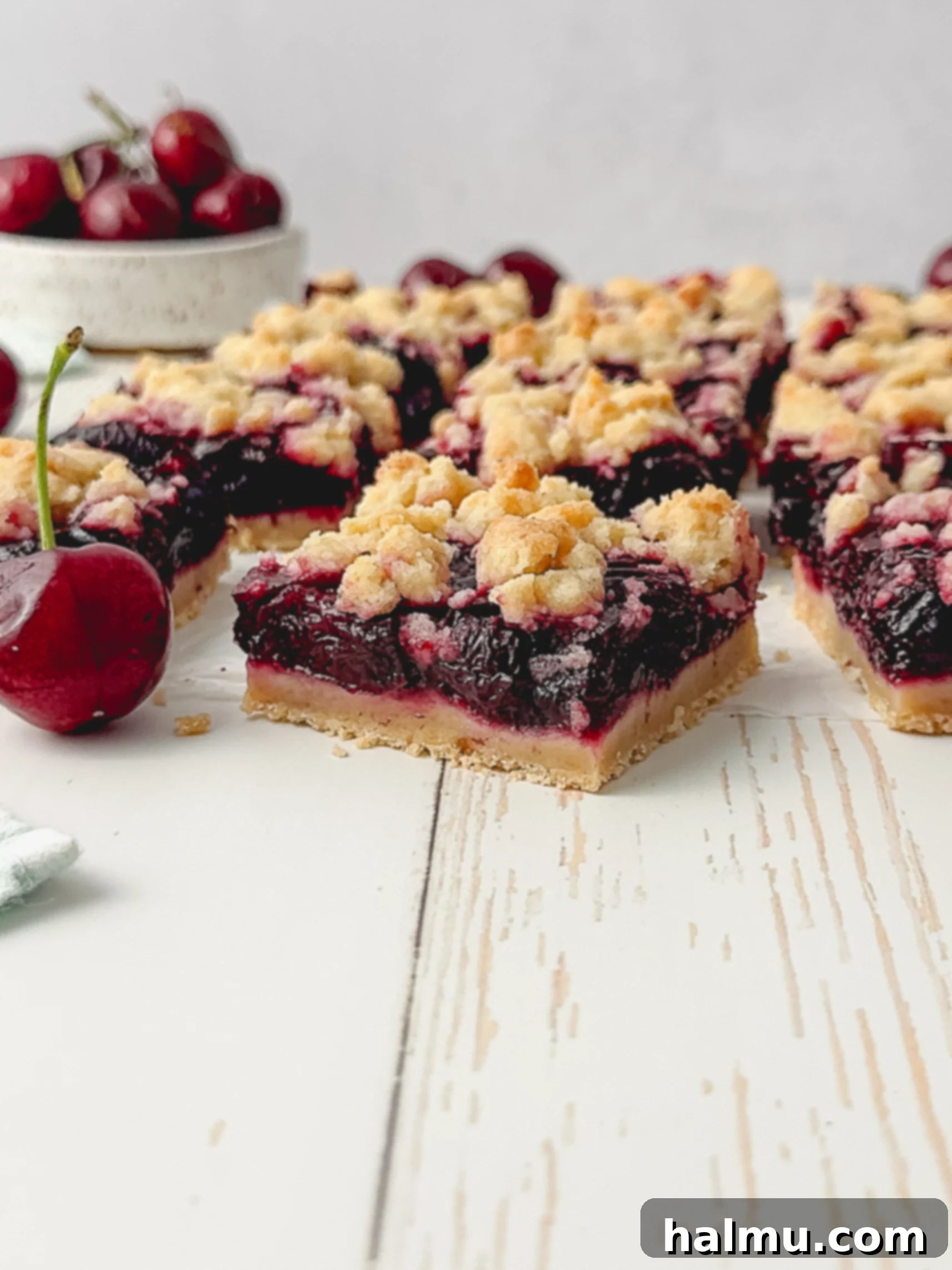 A slice of cherry crumb bar on a plate, with a fork, ready to be eaten.
