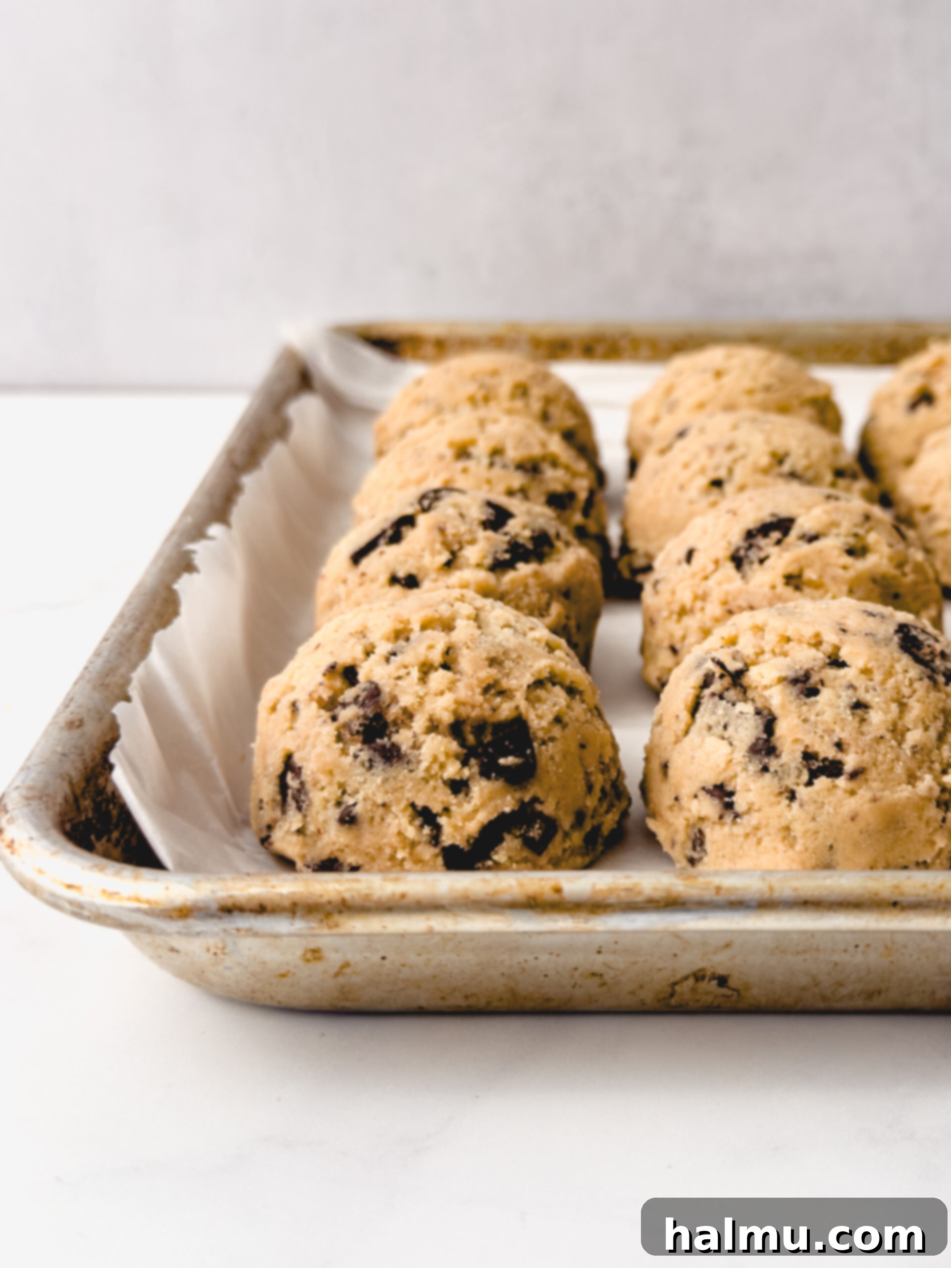 Scoops of chocolate chip cookie dough chilling on parchment paper.