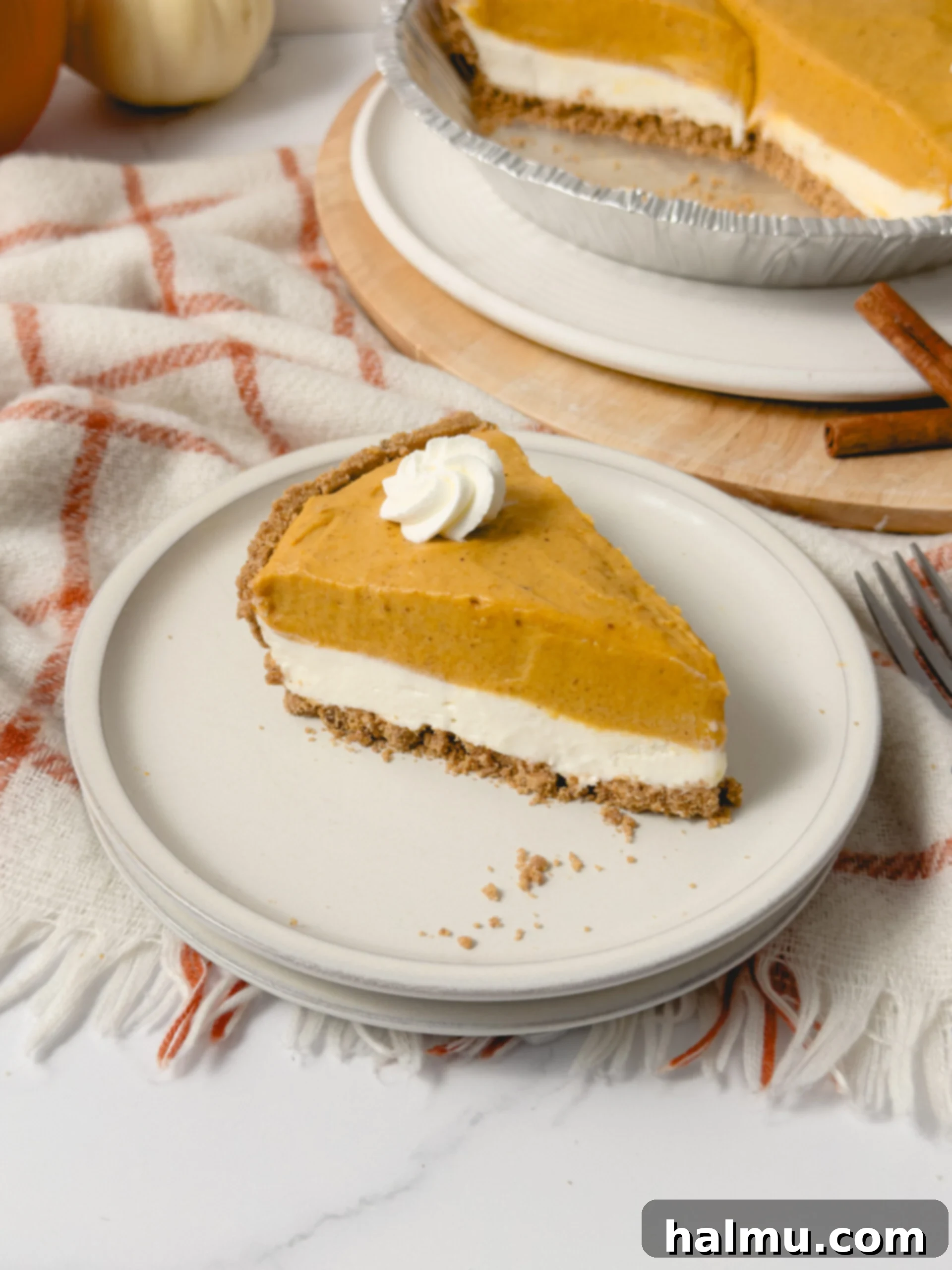 A slice of double layer pumpkin pie on a white plate, showcasing a creamy white layer and a smooth orange pumpkin layer on a graham cracker crust.
