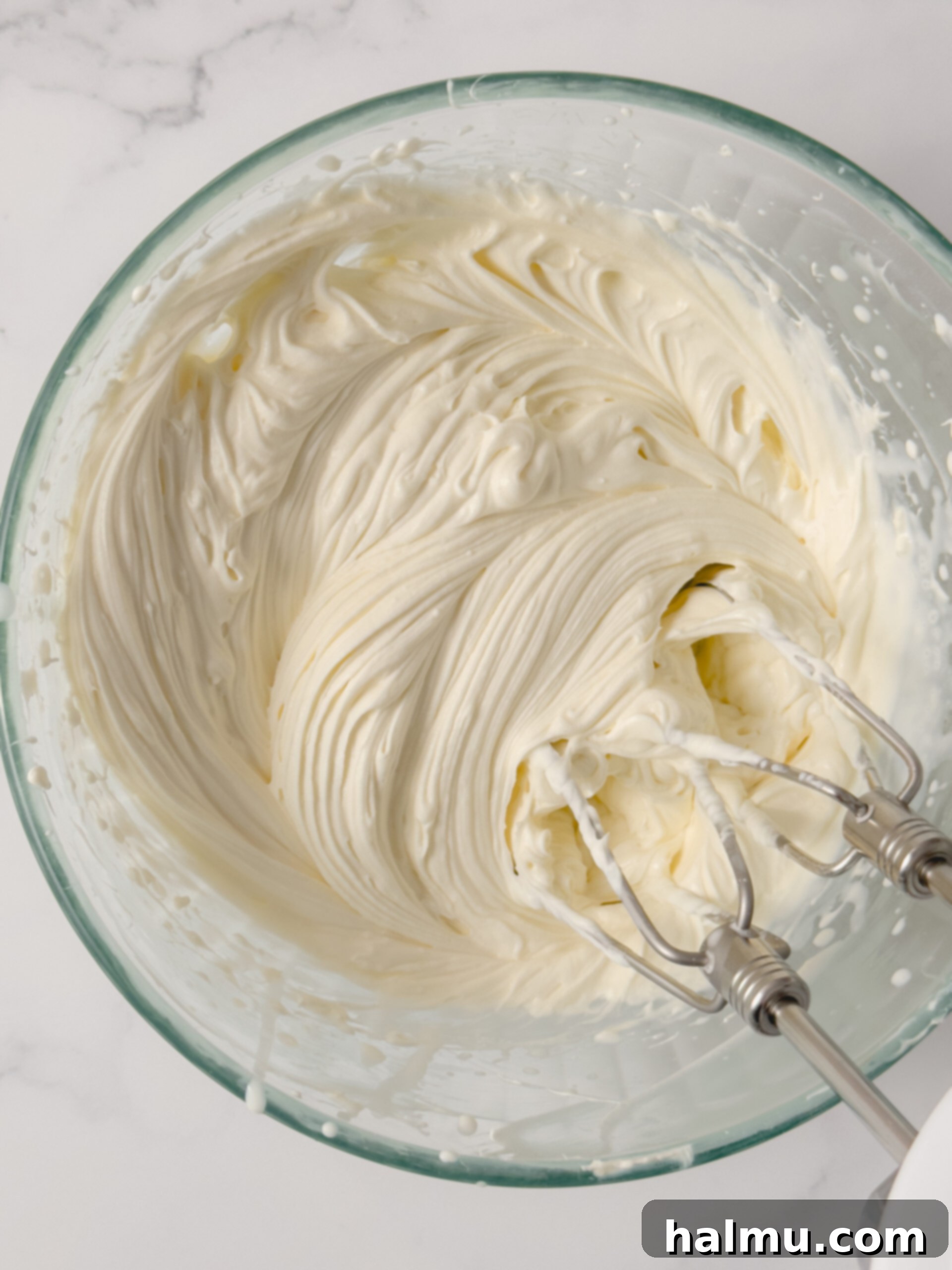 Cream cheese whipped cream being mixed in a bowl with an electric mixer.