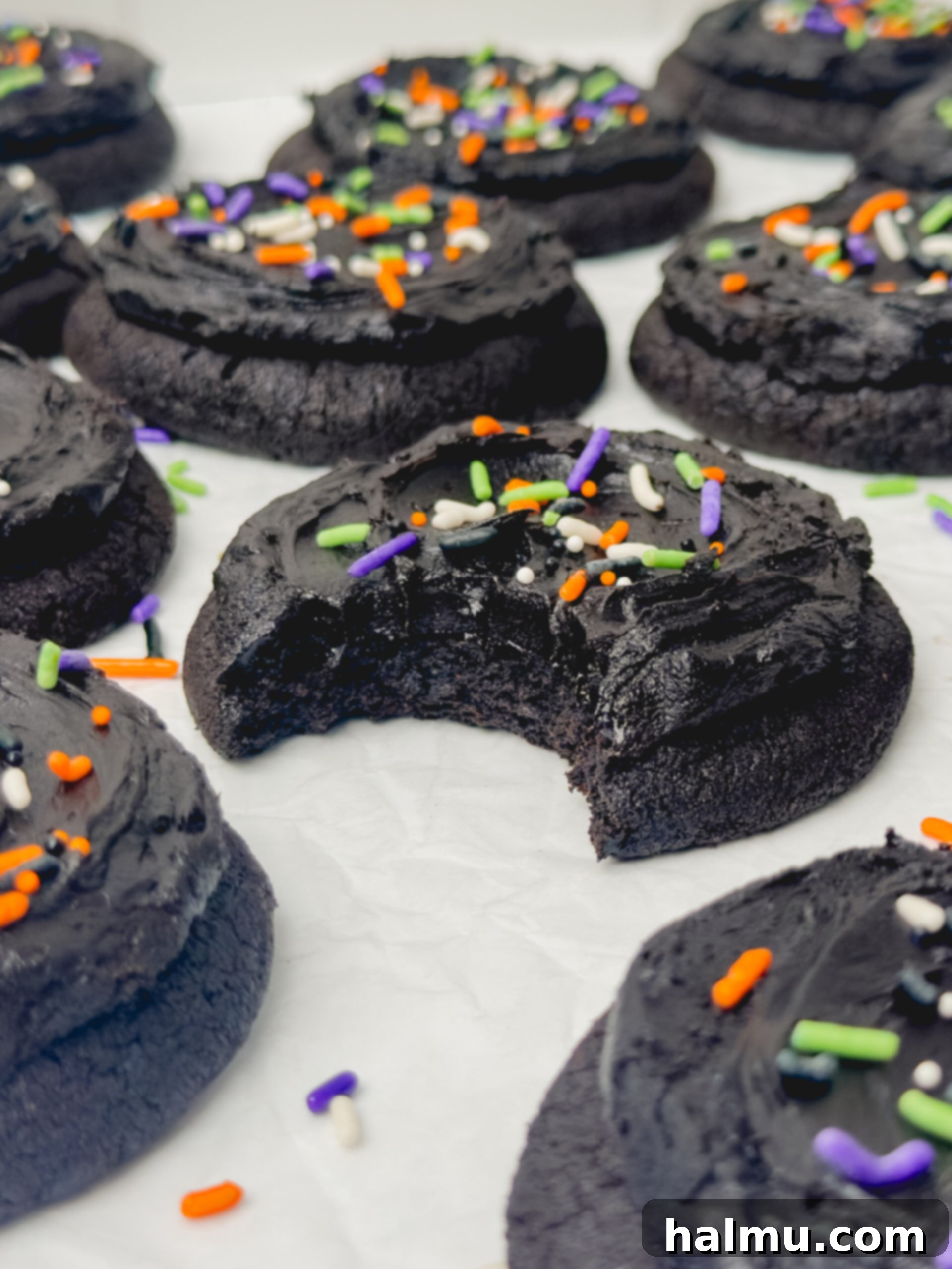 A delicious Frosted Black Cocoa Cookie broken in half, revealing its moist, fudgy interior and thick frosting.