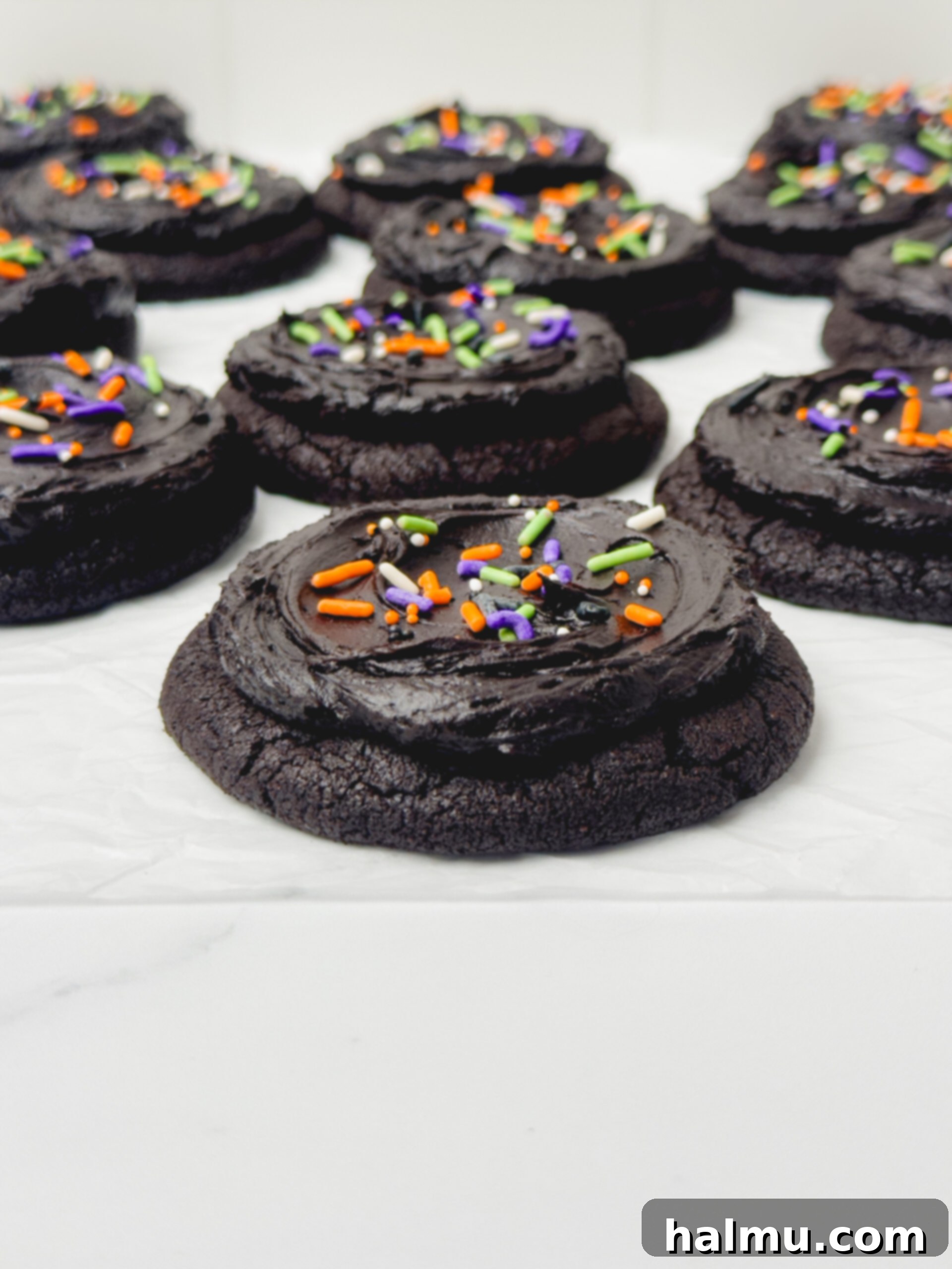 Two freshly baked Frosted Black Cocoa Cookies on a cooling rack, showing their deep black color before frosting.
