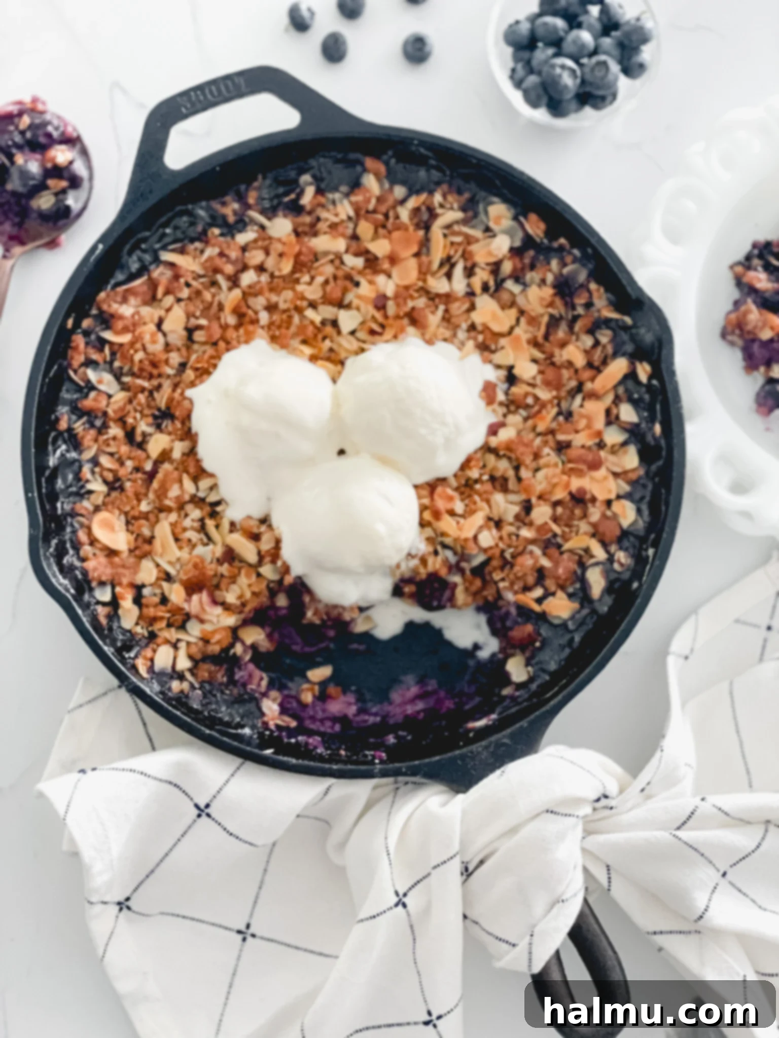 Delicious Blueberry Almond Skillet Crisp, golden brown with blueberries bubbling at the edges, served in a cast iron skillet, with a side scoop of vanilla ice cream.