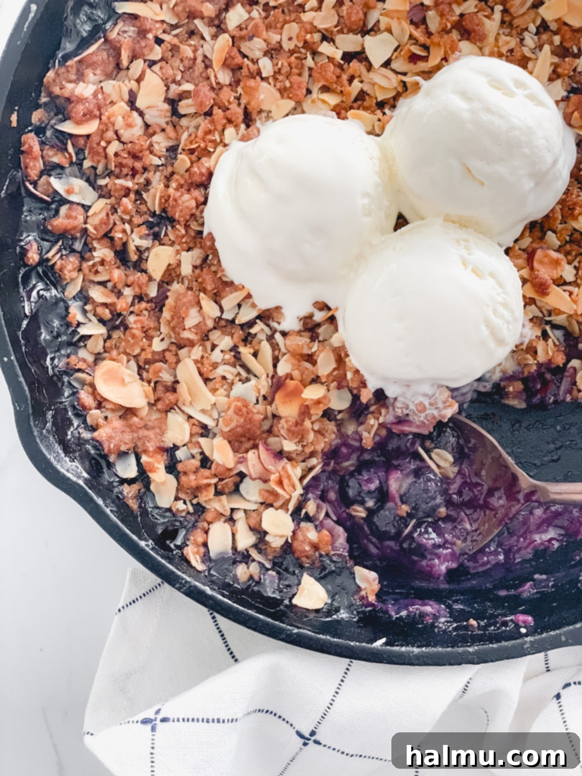 Close-up of the gooey, rich blueberry filling of the Skillet Crisp, with a spoon poised to scoop a portion.
