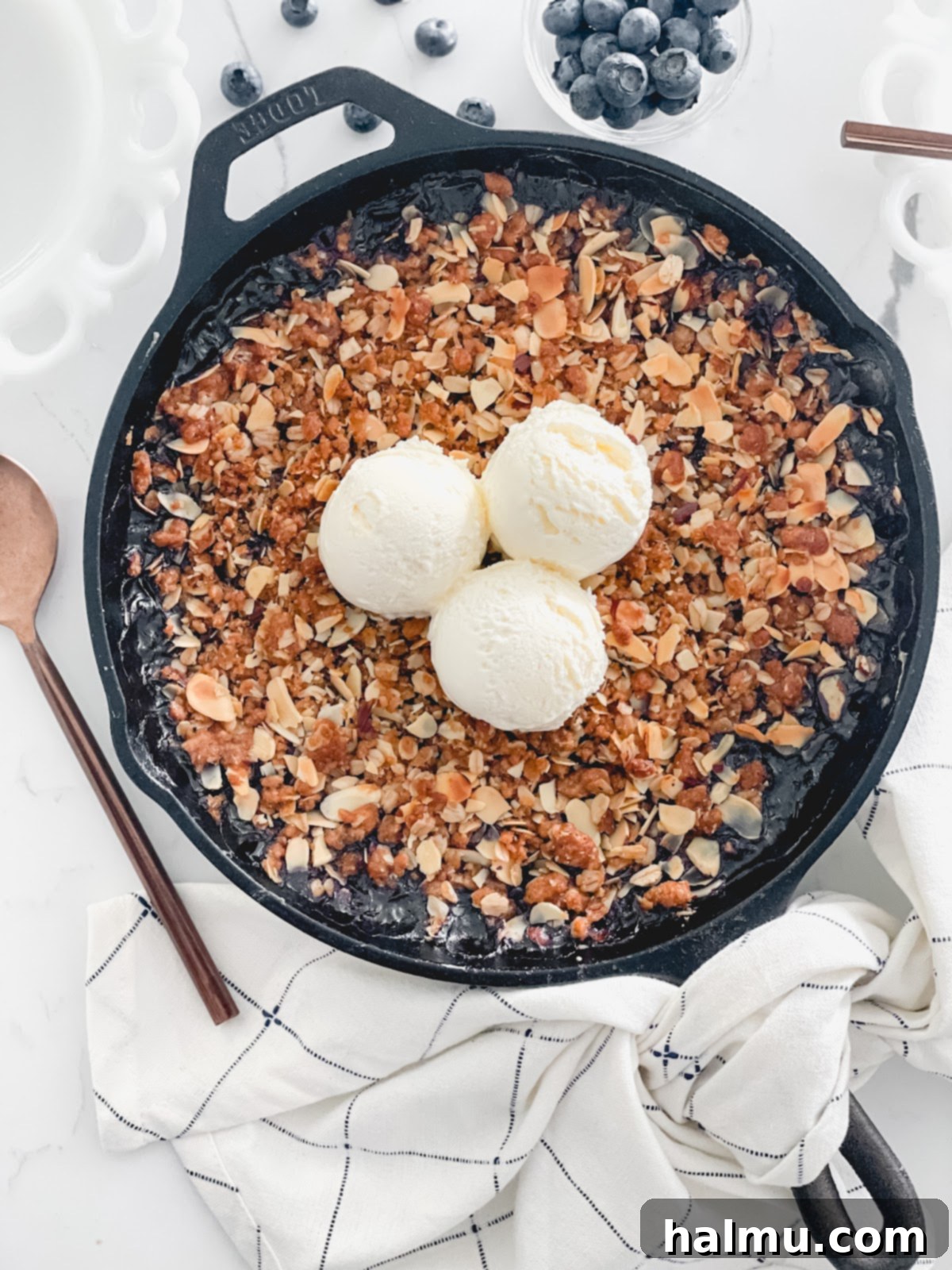 A serving of Blueberry Almond Skillet Crisp in a rustic bowl, generously topped with a scoop of melting vanilla ice cream, ready to be enjoyed.